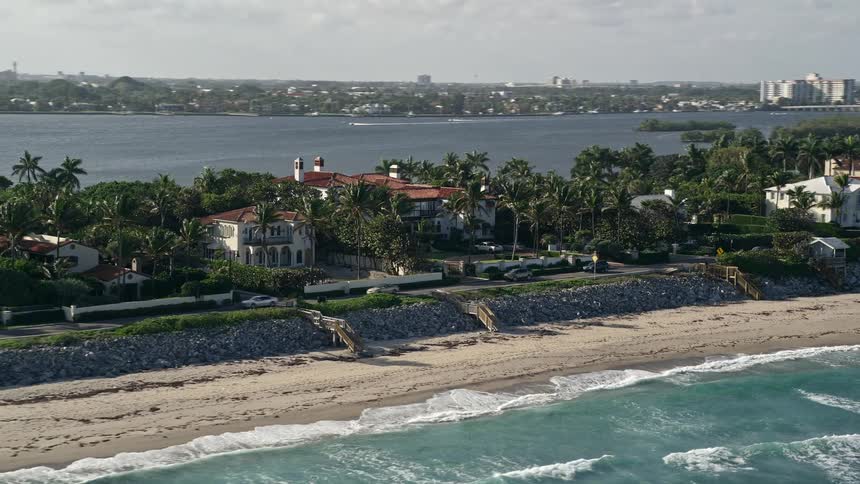 Aerial flyby footage showcasing luxurious mansions along the beachfront of Palm Beach Florida during the day