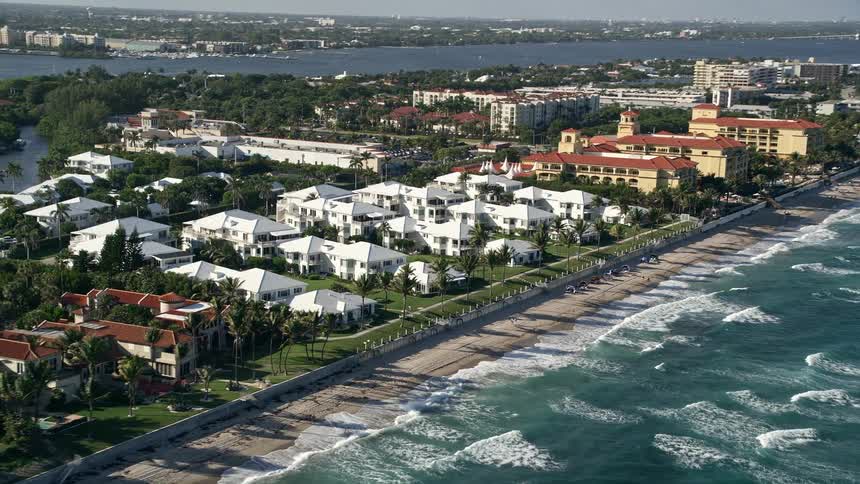 Aerial footage flying by beachside villas in Manalapan Florida overlooking the coastline and sea on a partly cloudy day with some sunbathers