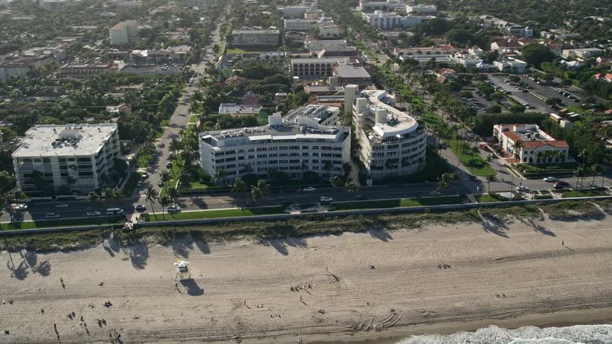 An aerial view of condominium complexes by the beach in Palm Beach Florida during the daytime with partly cloudy skies and shorelines dotted with sunbathers