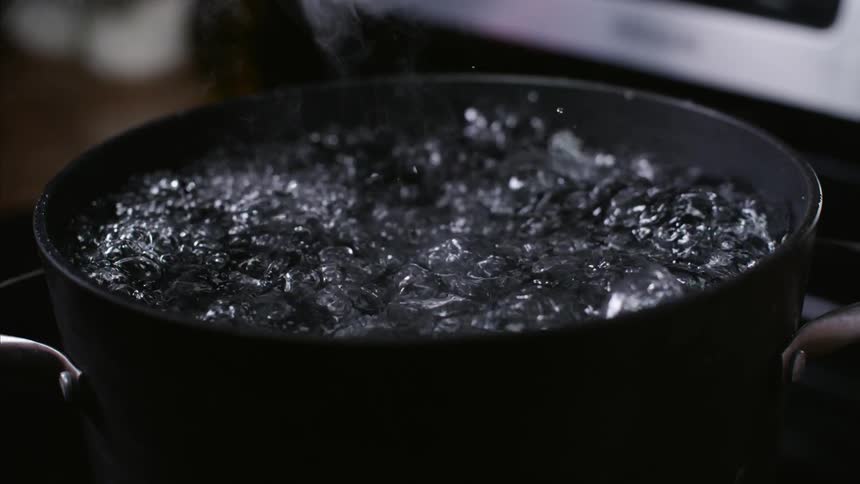 Someone lifting the lid off a pot of boiling water
