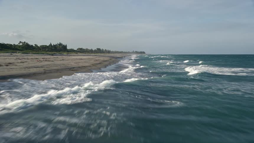 Flying over Hobe Sound Floridas empty beach this aerial footage reveals large waves crashing onto the shoreline on a partly cloudy day in summertime