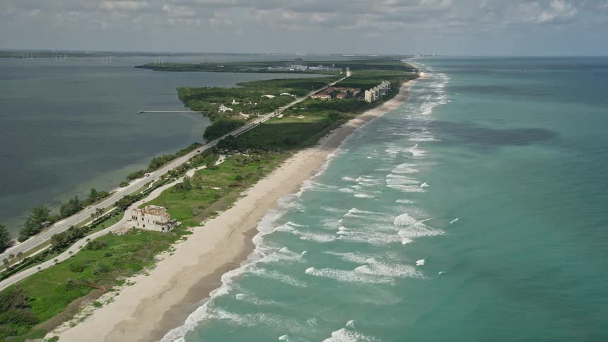 5K aerial footage of Jensen Beach Florida coast; flying over the oceanfront properties and beach without people under partly cloudy skies during spring or summer