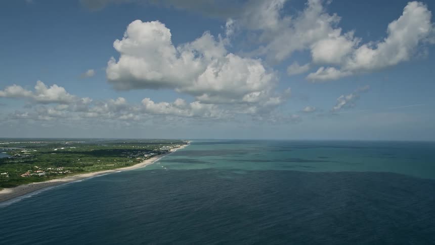 Approaching Vero Beach from high above the ocean on a partly cloudy day with an aerial view of the shoreline and empty beach