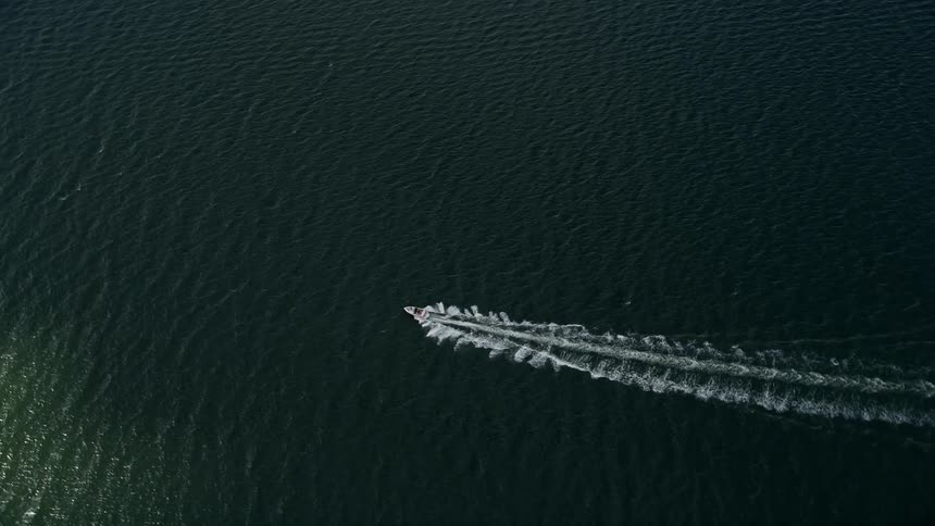 A speedboat cruises through the river leaving waves behind it in Melbourne Beach Florida captured by 5K aerial footage and taken during summer daytime for transportation relaxation and water sports
