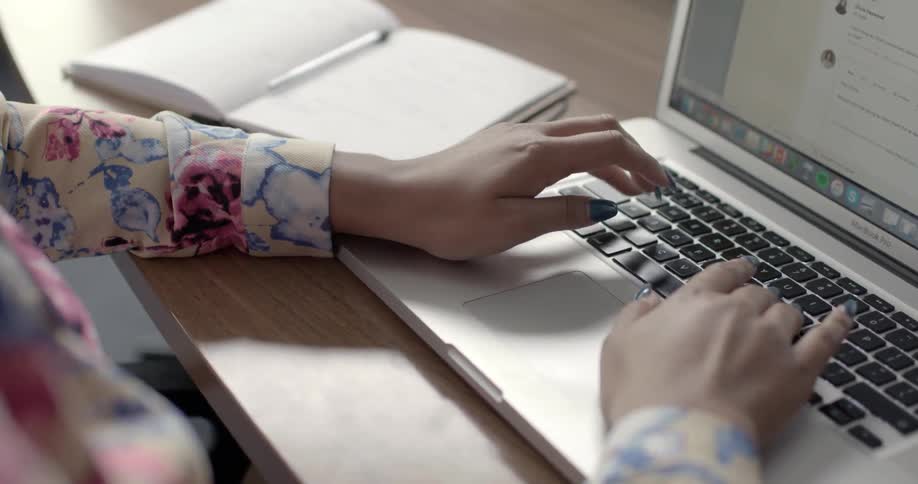 A woman sitting at a desk is typing on a mac book pro
