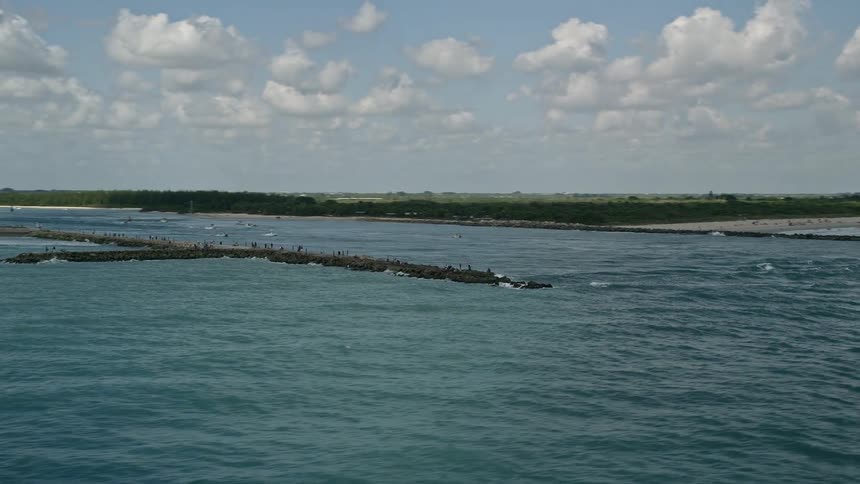 Aerial view of boats approaching the breakwater and sailing through the inlet at Fort Pierce Florida with a partly cloudy sky in the background