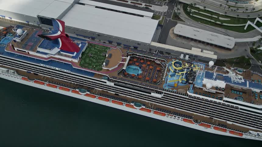 An aerial approach and tilt down to a docked Carnival Cruise Ship in Port Canaveral Florida waiting for passengers under partly cloudy skies during the summer months