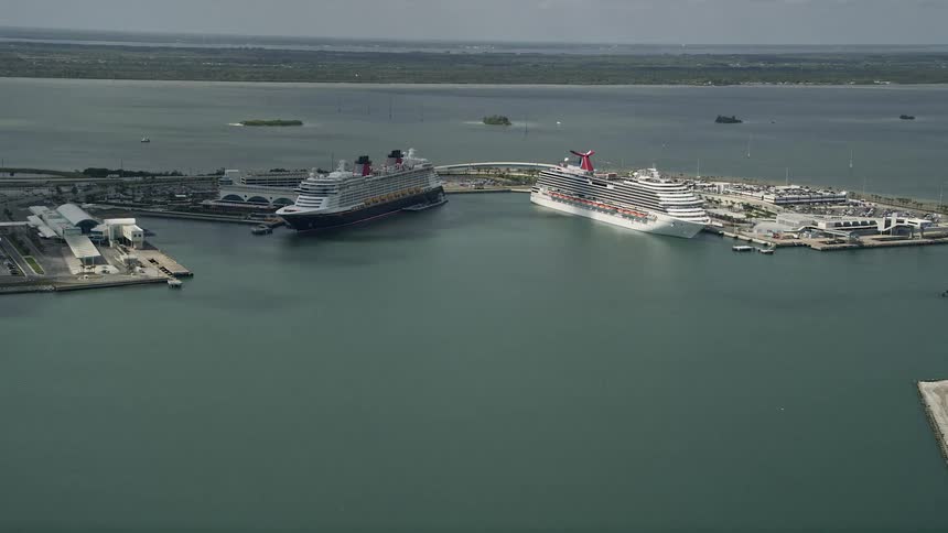 Approaching Carnival and Disney cruise ships docked at Port Canaveral on a partly cloudy day as seen in an aerial view during summer from the Florida Aerials shoot