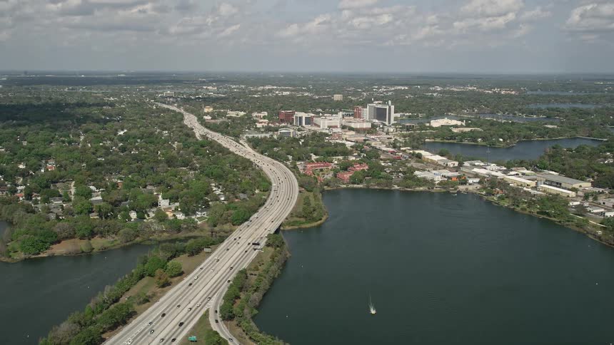 Aerial view of a Florida interstate beside a lake with a light traffic and partly cloudy skies