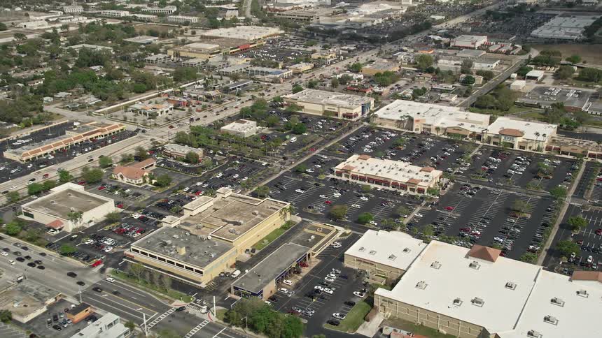 Approaching a shopping mall and parking lot from an aerial with partly cloudy skies in Orlando Florida during daytime