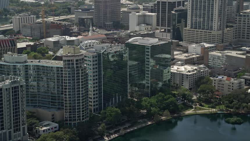 Fly over Downtown Orlandos diverse skyline featuring office buildings and luxury condos resting on the shores of Lake Eola