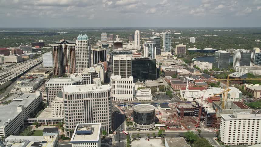 An aerial view of Downtown Orlando and the Spessard L Holland East West Expressway while approaching Lake Lucerne and revealing the shoreline on a partly cloudy day in Florida