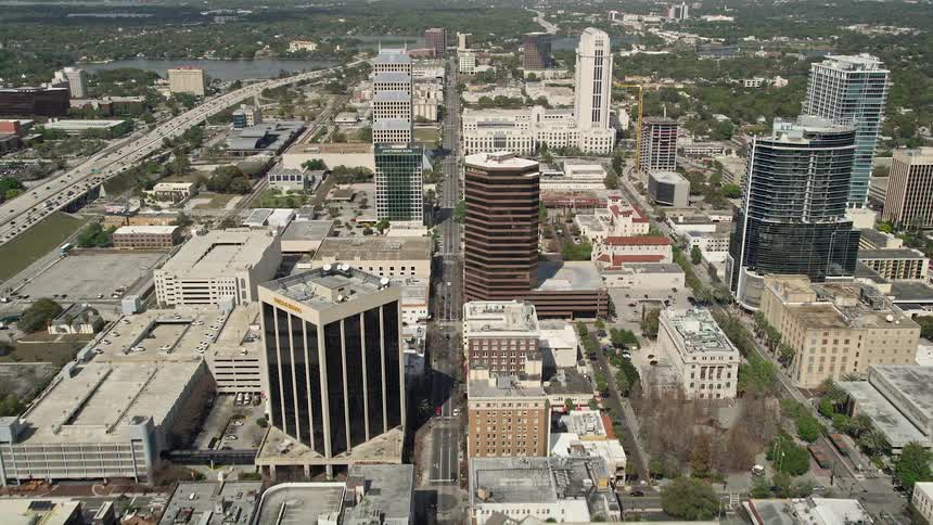 An aerial shot follows Orange Avenue through Downtown Orlando capturing the skyscrapers and city streets below