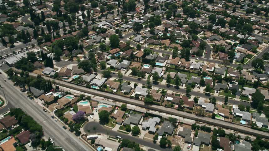A sunny reverse aerial view of a Southern California suburban neighborhood with trees houses and pools in West Hills Los Angeles