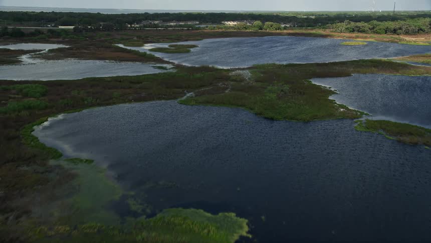 Aerial flyover of waterfront homes and patches of grassy land towards open water in Florida with partly cloudy skies