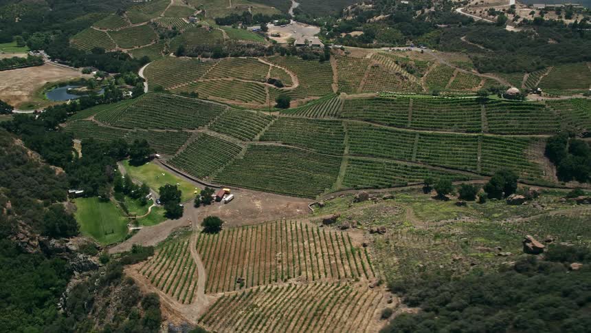 Approaching and flying over rustic rock formations to reveal sunny hilly vineyards in Malibu California