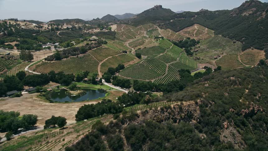 An aerial flyby in Malibu California showcasing rock formations vineyards and a country road surrounded by hills