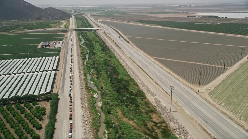 Aerial footage of cars traveling on a dirt road past crop fields and greenhouses on South Lewis Road in Camarillo California