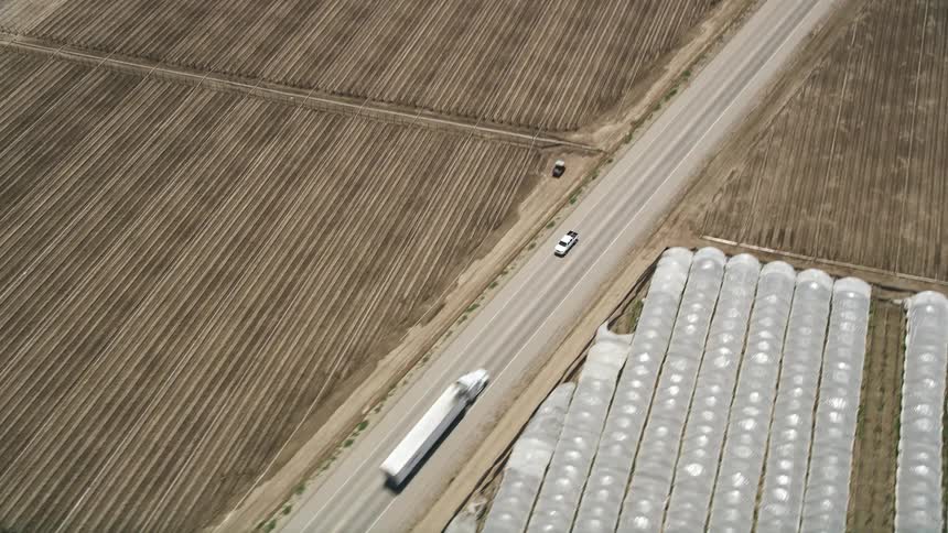 A white truck travels down a country road between farm fields seen from an aerial view