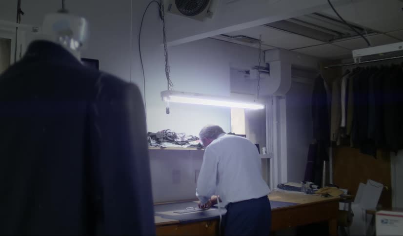 Tailor with white shirt and dark blue pants works at dressmaker workshop