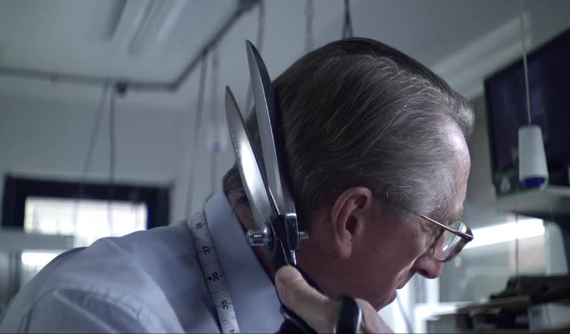 Tailor with measuring tape around his neck wipes tailor shears against his hair
