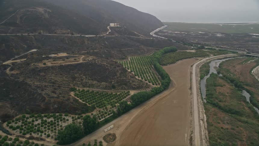 Approaching rustic orchards and farmland near a hazy country road at the base of mountains in Californias Point Mugu area