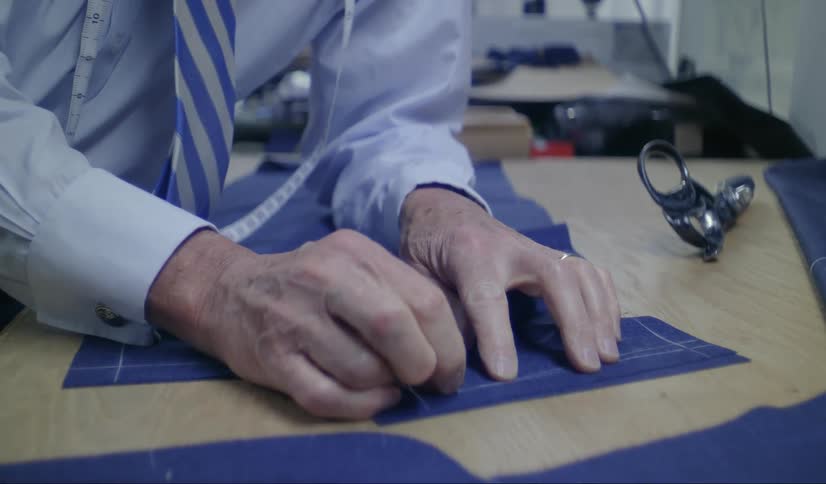 A close up of a mans hands sewing blue material together on a wood table
