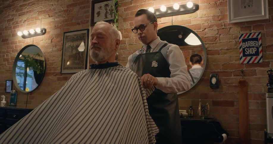 A barber puts a protective cape on a client sitting in his salon chair