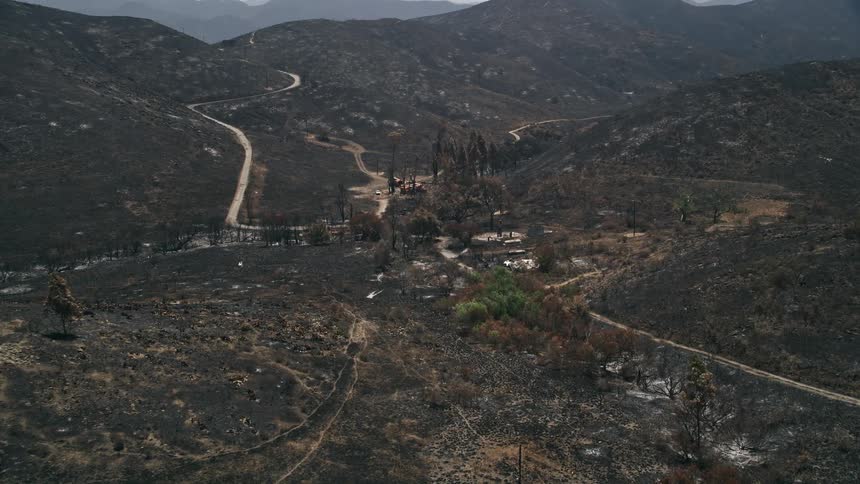 Aerial footage of fire-ravaged rural homes and neighborhoods surrounded by wildfire damage in the Santa Monica Mountains California