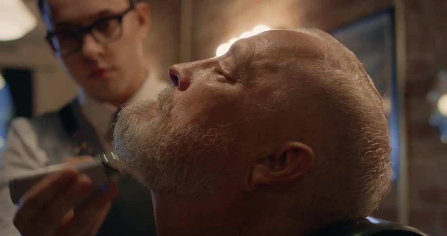 A man gets his beard trimmed by a barber