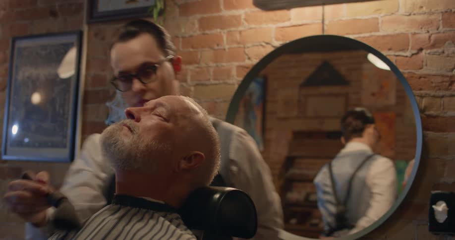 A barber softly brushing off his customers face as the customer sits in the chair with his eyes closed
