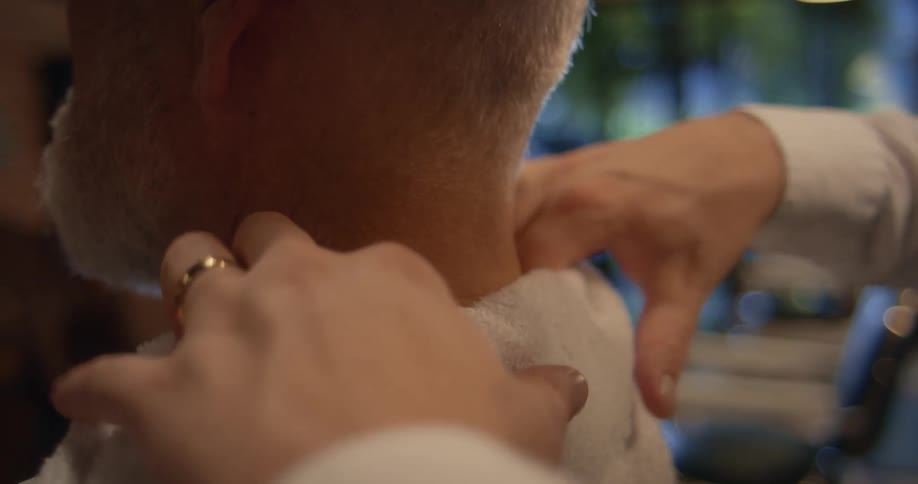Barber with white shirt tucks towel around mans neck in the barbershop