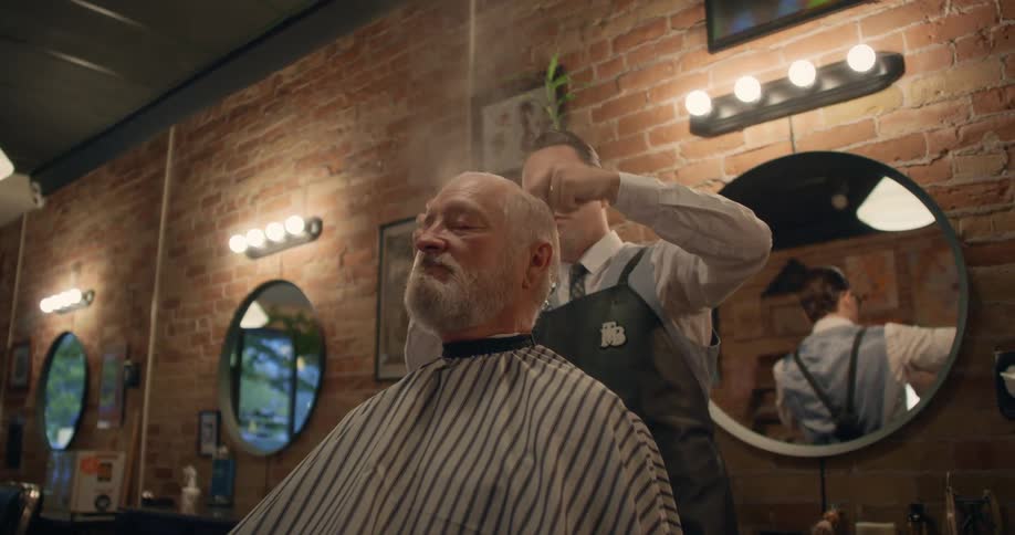 A barber sprays and combs the hair of a customer in a barber shop during the day