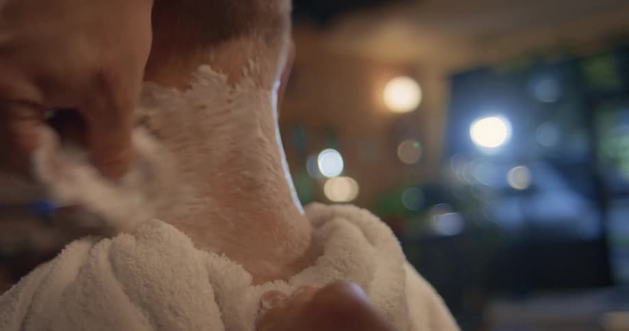 A close up of a mans neck having shaving cream brushed on it by a barber