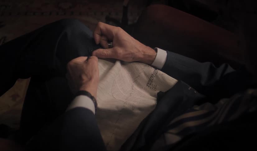 Man wearing business suit stitches hem while sitting in chair
