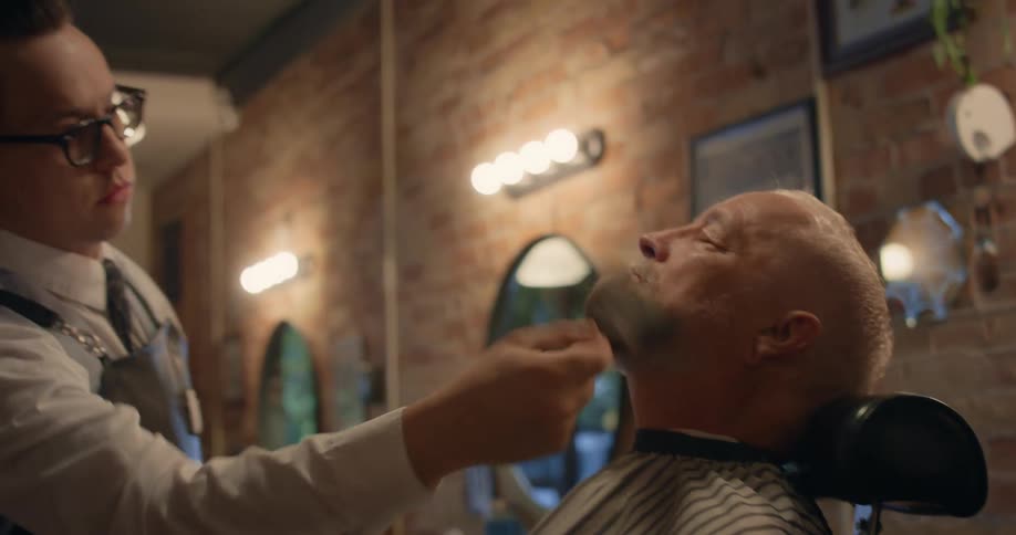 Barber brushes hair off skin and haircut covering worn by client sitting in barber chair