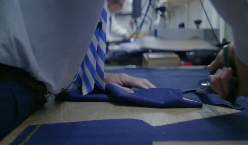 Tailor with blue shirt and pants cuts cloth with scissors at workshop