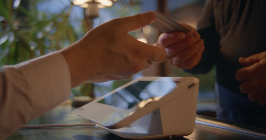 Someone behind a counter infront of a glass doorwindow enters information via a touchscreen and then is handed a credit card by the man on the other side of the counter