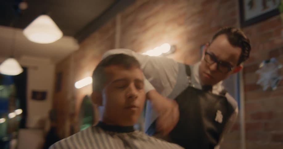 A barber is brushing cut hair away from a young mans neck and cape