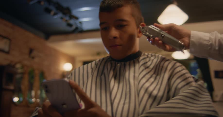 A barber combs a young mans hair and trims it with an electric razor