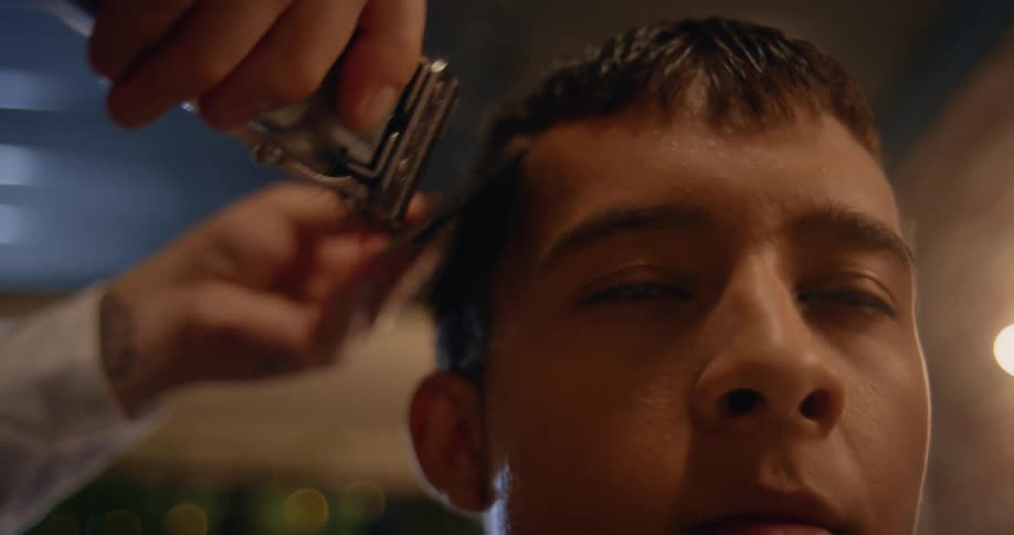 A barber uses a razor and comb to cut a mans hair