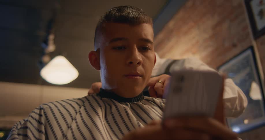A male barber trims a young mans hair with an electric razor