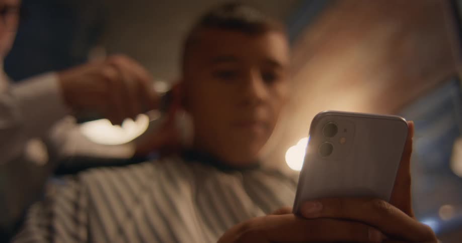 Barber trims client hair as the client scrolls on hissmartphone