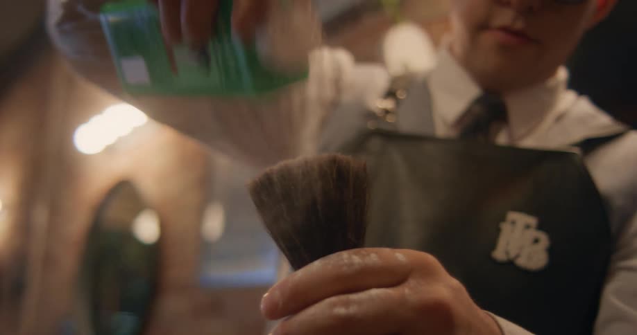 A barber dumping powder on a brush in his hand while smiling