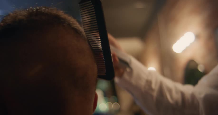A close up of a barber using a comb and clippers on a customers head as he looks it over up and down