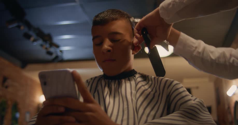 Customer gets a haircut at a barber shop while on his phone