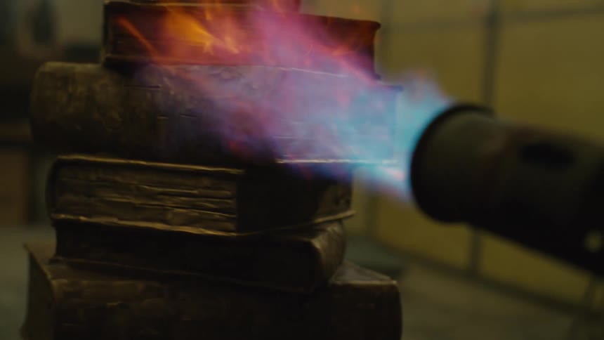 A person using a torch to a flame on a stack of steel books