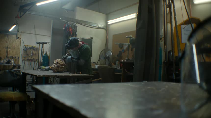 A worker wearing a protective face shield focuses on their project