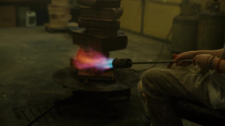 A metal sculptor using a torch to work on a sculpture of stacked books