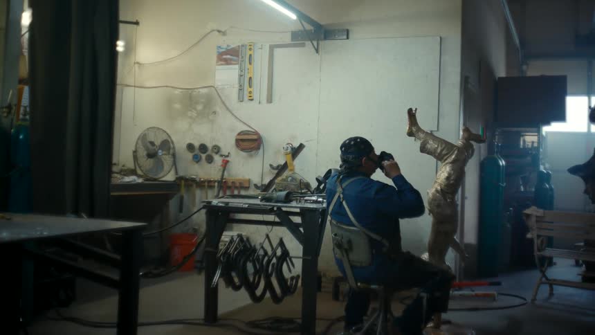 A sitting metal sculptor puts on a mask as he prepares to work on a metal statue